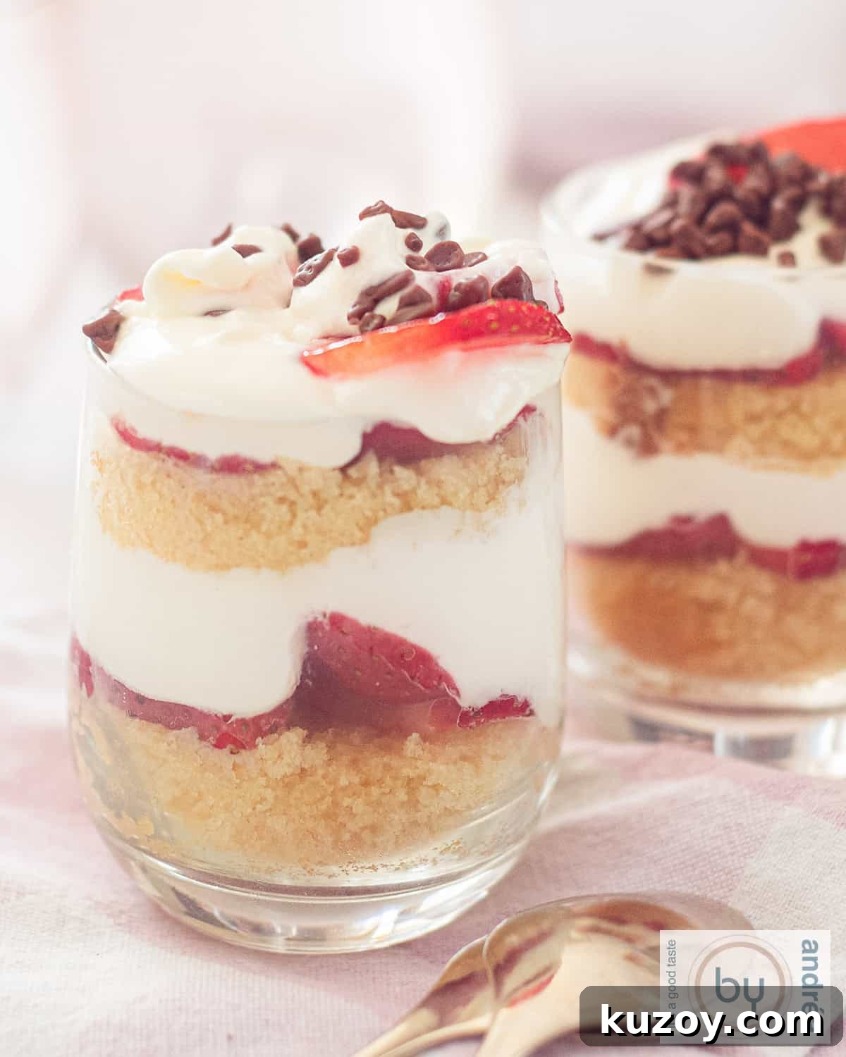 A height photo with two glasses filled with layers of cake, fresh strawberries, mascarpone cream alternating