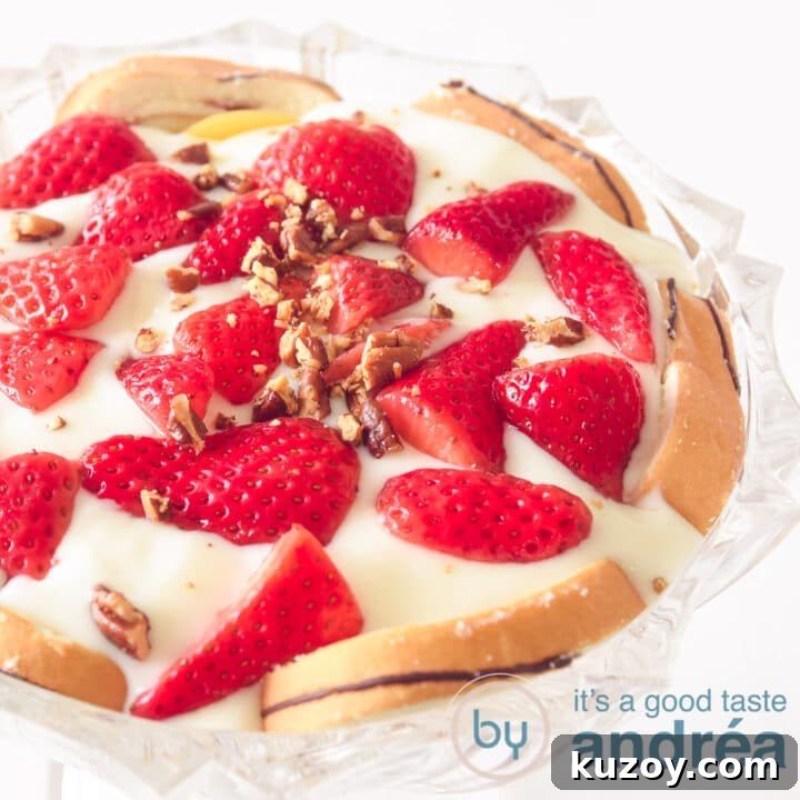 A square photo with a glass bowl filled with layers of cake, cream, strawberries and pecans