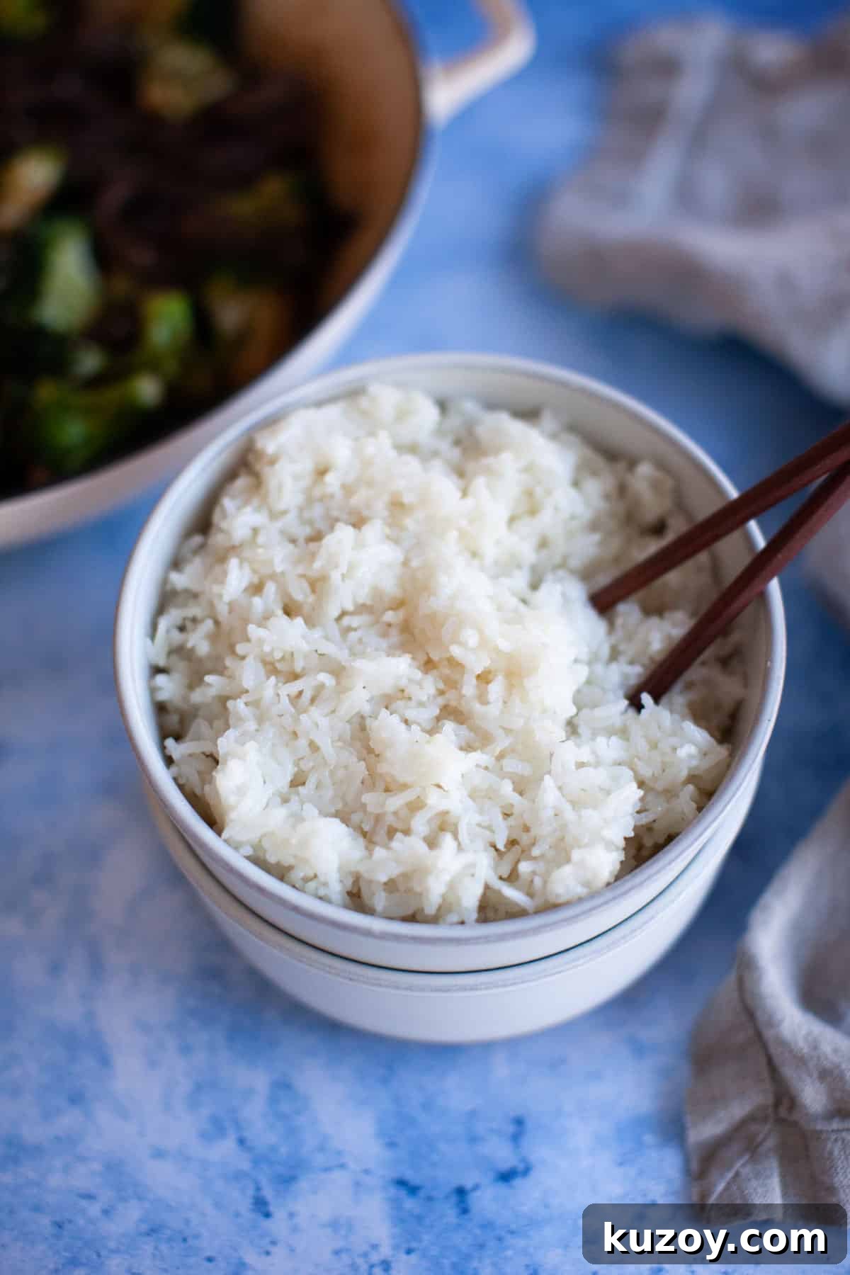 Overhead shot of plain white jasmine rice in a white bowl on a blue countertop.