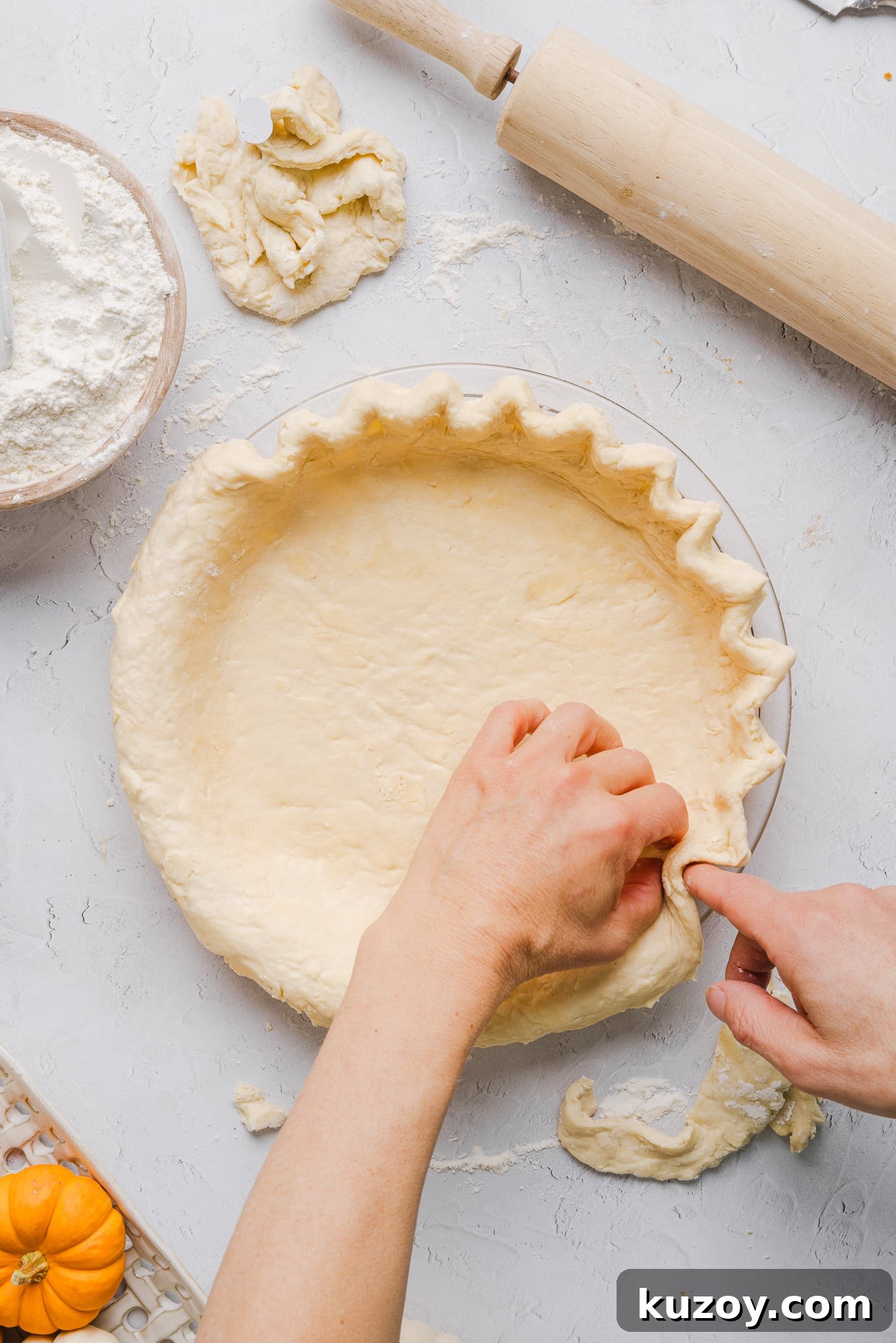 Healthy pumpkin pie crust being added to the pie pan and edges being crimped.