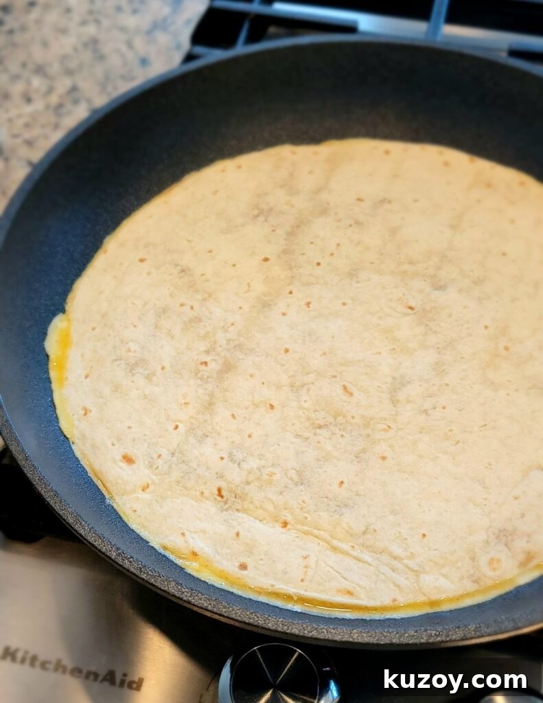 Tortilla placed over cooking eggs in pan