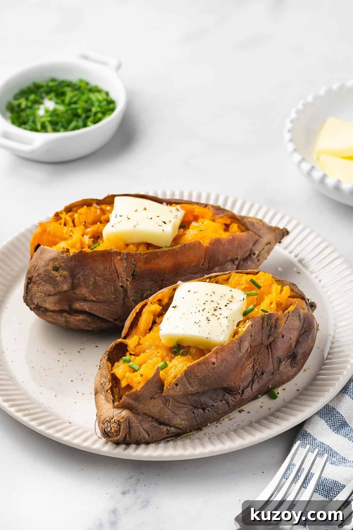 A plate with two slow cooker sweet potatoes with butter and chives on top.