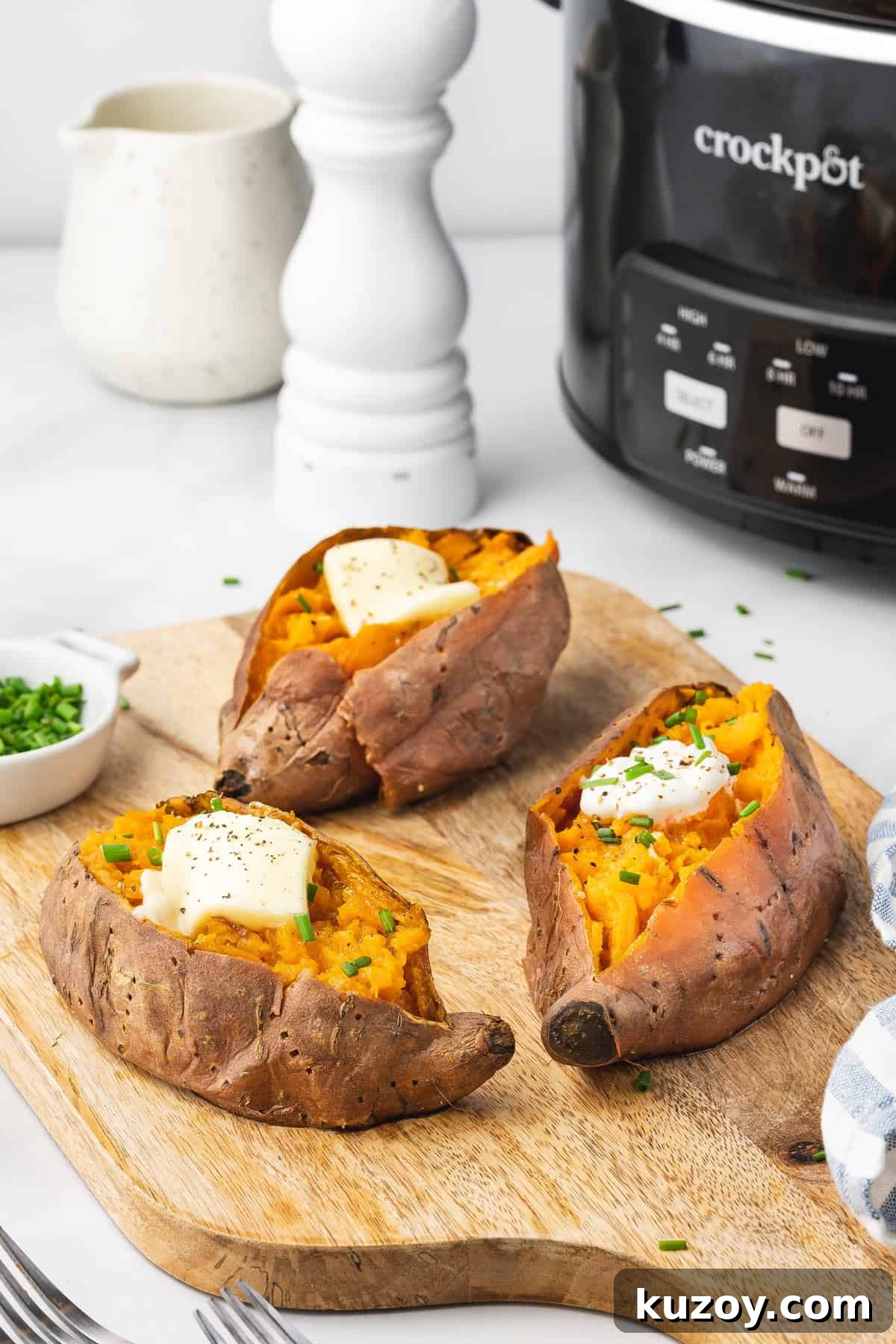 Three slow cooker sweet potatoes with butter and chives on top.