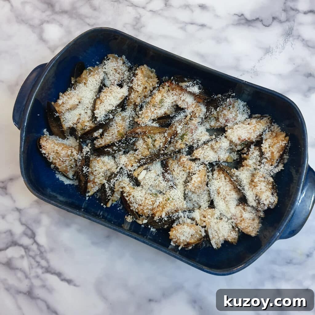 Stuffed mussels in a blue baking dish, sprinkled with grated parmesan cheese.