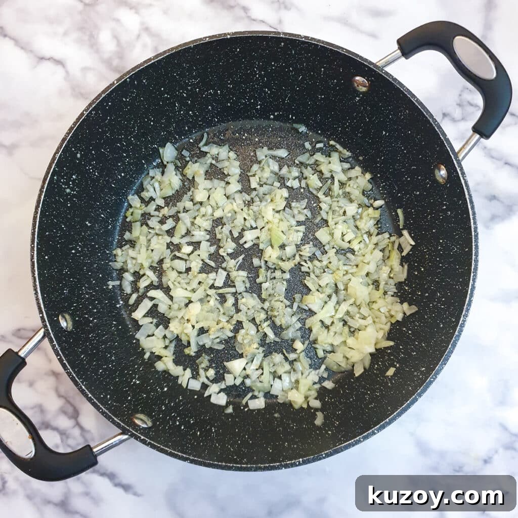 Chopped onions being softened in a large frying pan.