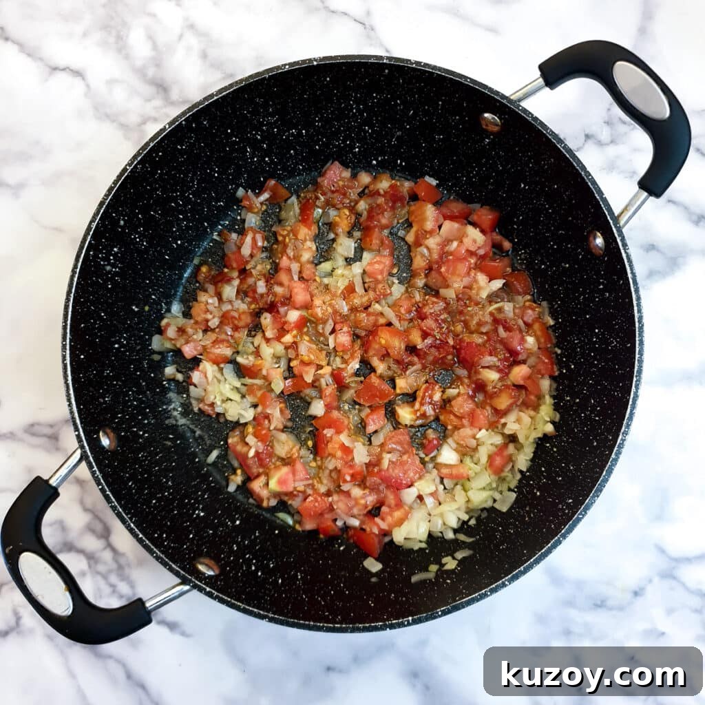 Chopped tomatoes added to onions in a frying pan.