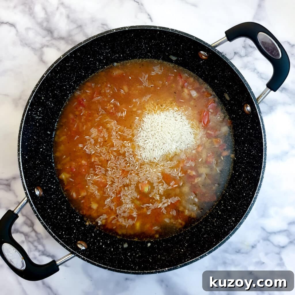 Water, rice and spices added to onions and tomatoes in a frying pan.