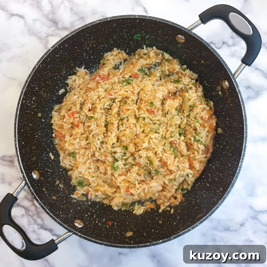 Cooked tomato rice in a frying pan with chopped fresh herbs stirred through.