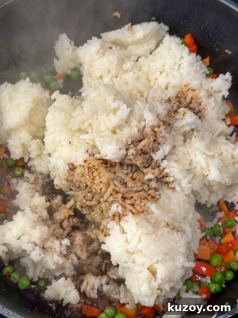 Soy sauce poured over cooked white rice being added to sautéed vegetables in a deep skillet.