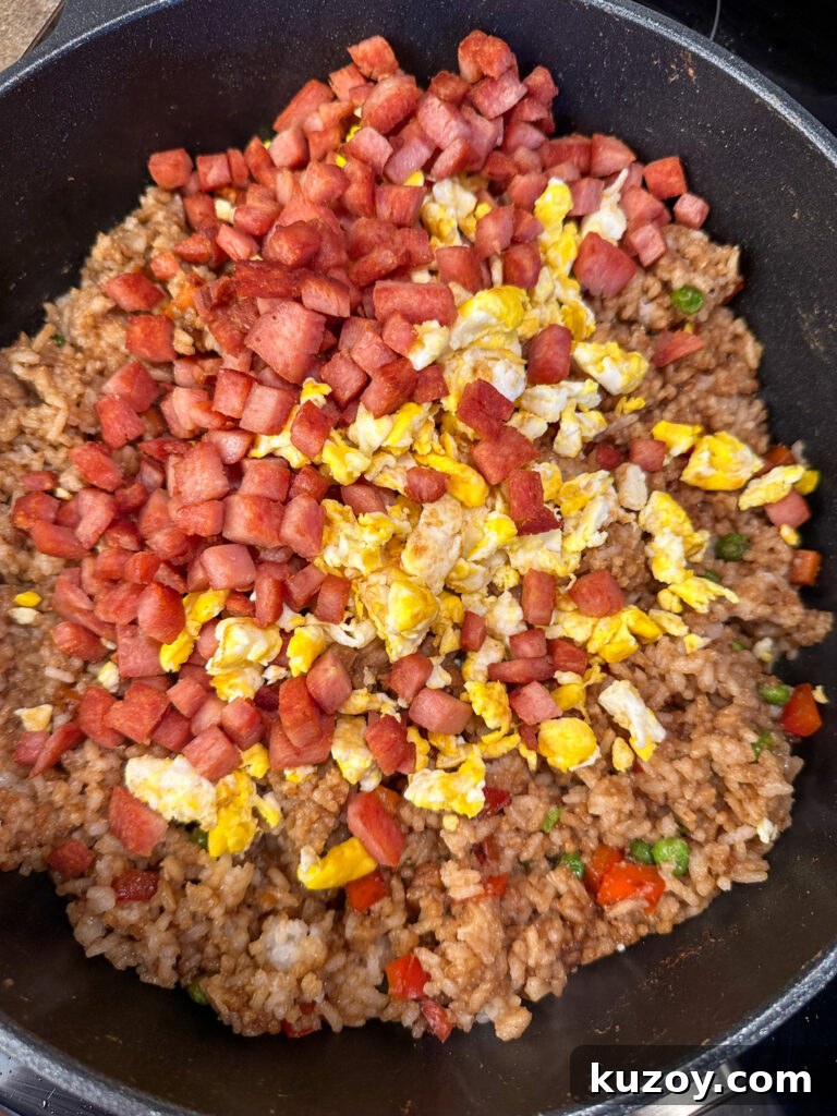 Chopped spam and scrambled eggs poured on top of vegetable fried rice in a black skillet.