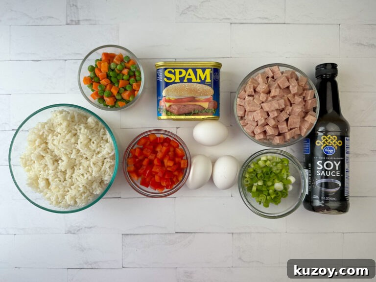 Ingredients to make spam fried rice are cooked white rice, frozen peas and carrots, a can of SPAM, chopped bell pepper, eggs, sliced green onions and soy sauce on a white counter top.