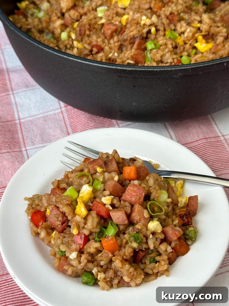 Overhead plate of fried rice with generous bites of browned spam nestled throughout with the skillet full in the background on a red and white napkin.