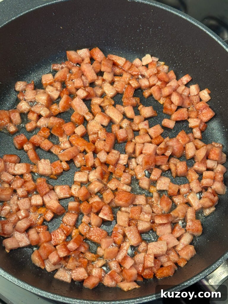 Small cubes of spam sizzling in a non-stick skillet.