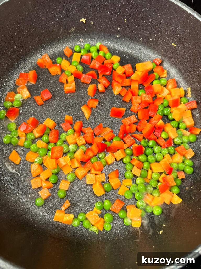 Chopped red pepper, carrots and peas in a hot skillet cooking in oil.