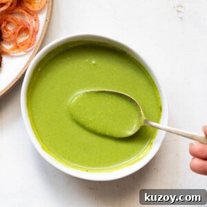mint chutney served in a white bowl with a spoonful of chutney being taken out