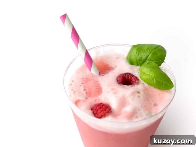 Cup of Raspberry Sherbet Punch with fresh raspberries, pink straw, and basil leaves