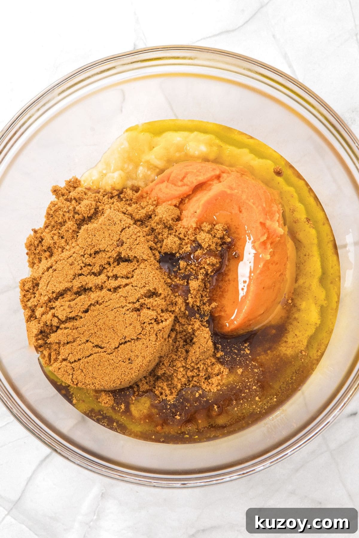 A glass bowl with sugar, pumpkin puree, oil and mashed bananas