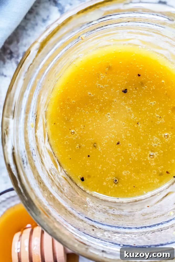 Overhead close up shot of honey mustard dressing in a glass mason jar on a white counter.