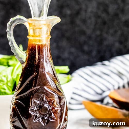 Glass bottle of balsamic vinaigrette on a white counter with salad in the background.