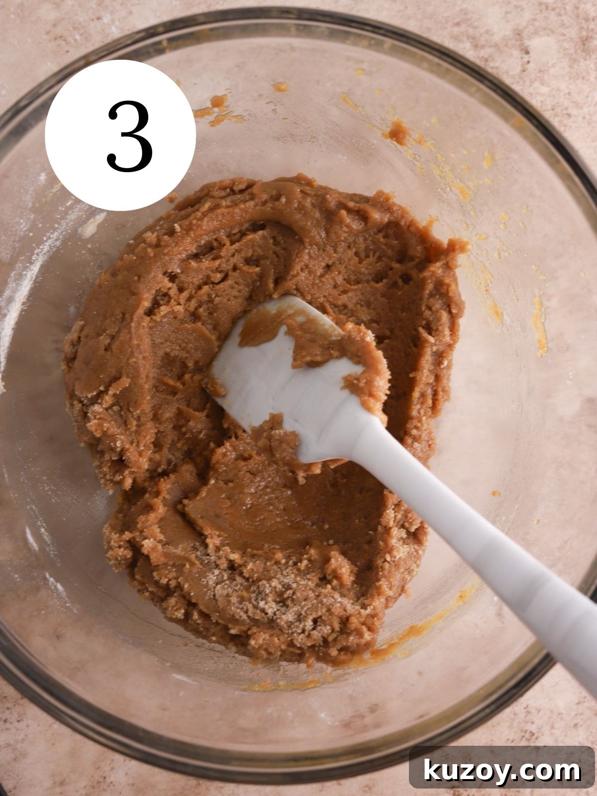 A glass bowl with dough for chai bars mixed together with a spatula.