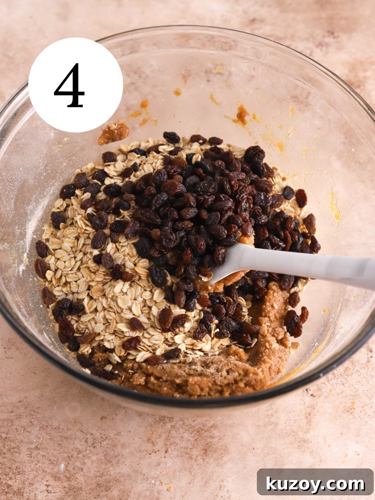 A glass bowl with oats and raisins being stirred into batter.