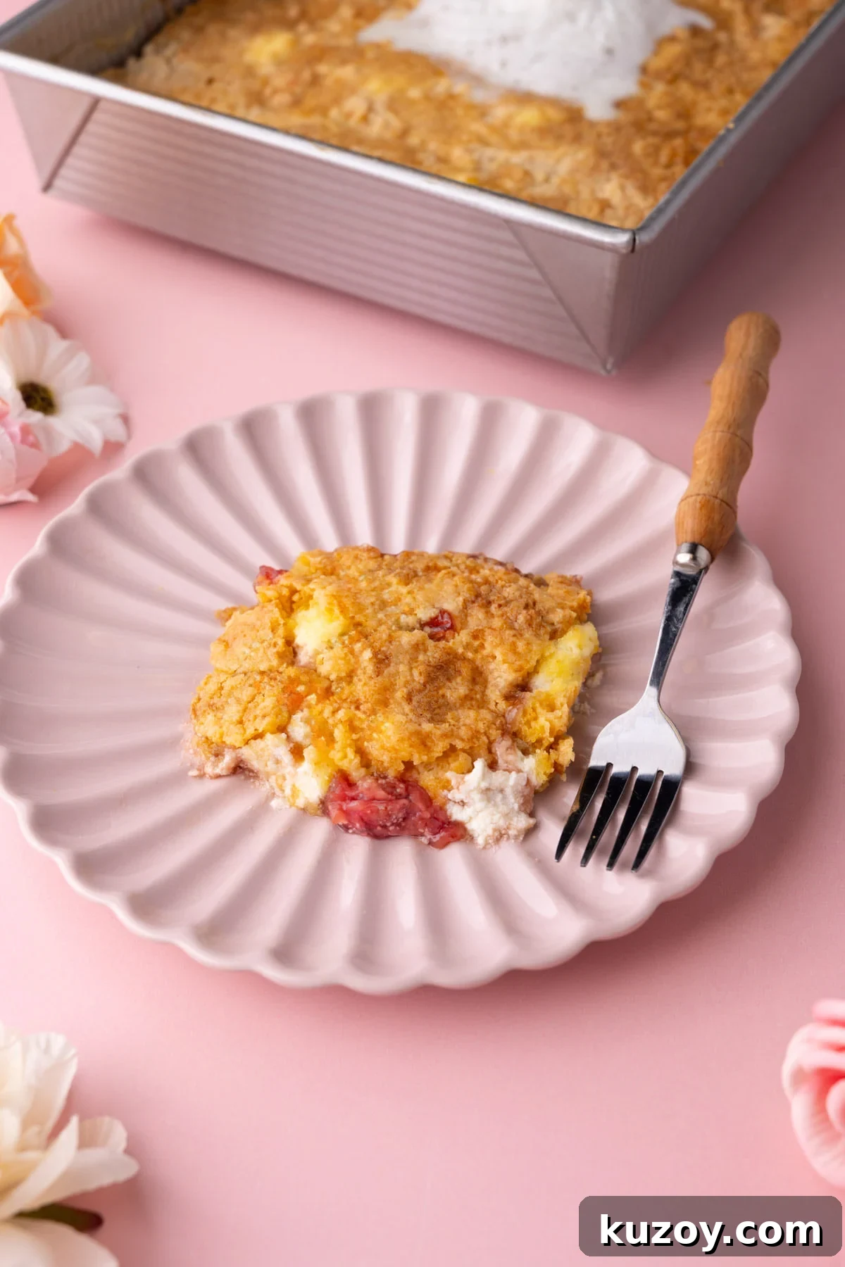 Serving of Strawberry Cheesecake Dump Cake on a pink scalloped plate with a fork. 