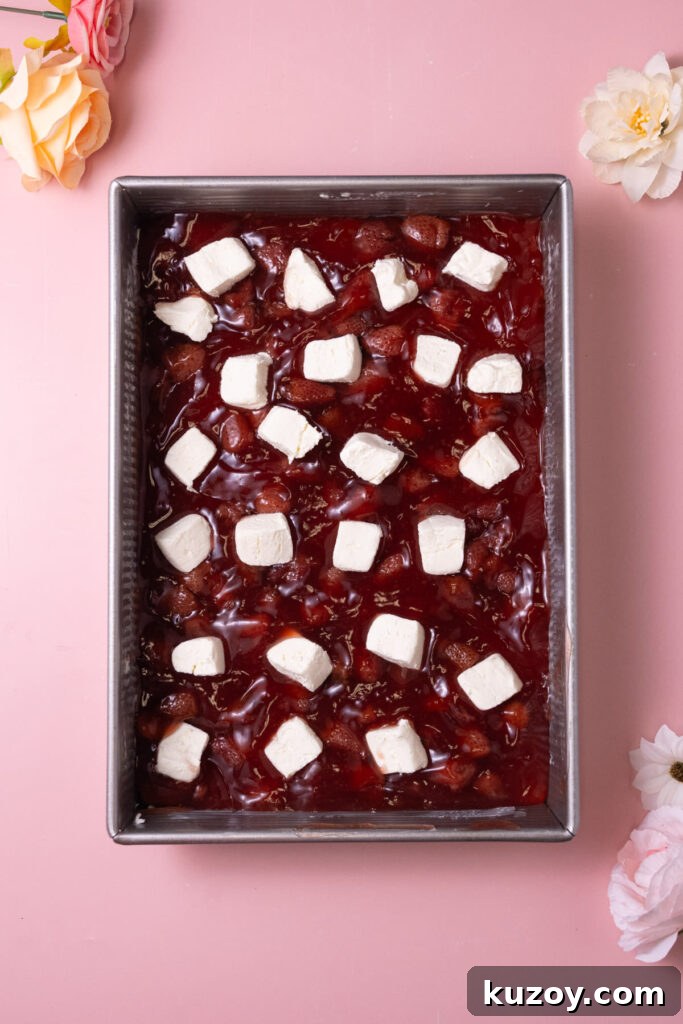 Dollops of cream cheese sporadically spread over strawberry fruit filling in a casserole dish. 