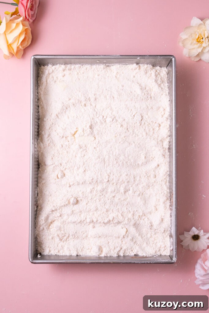 Boxed yellow cake mix spread over strawberry filling and cream cheese in a dish. 