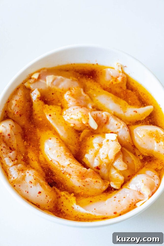 raw chicken tenders in a bowl with ajika seasoning and olive oil